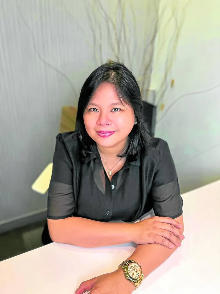 Rea Celine Villa seated at a table, smiling, arms folded